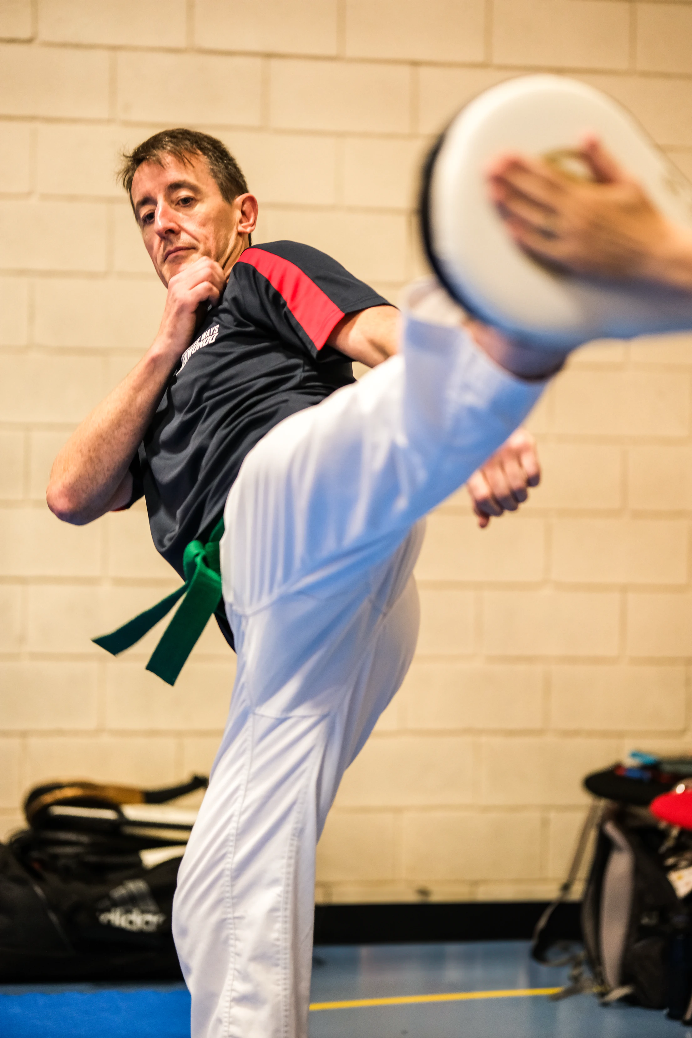 Adult student practising a high kick onto a pad during a Creative Ways Taekwondo class