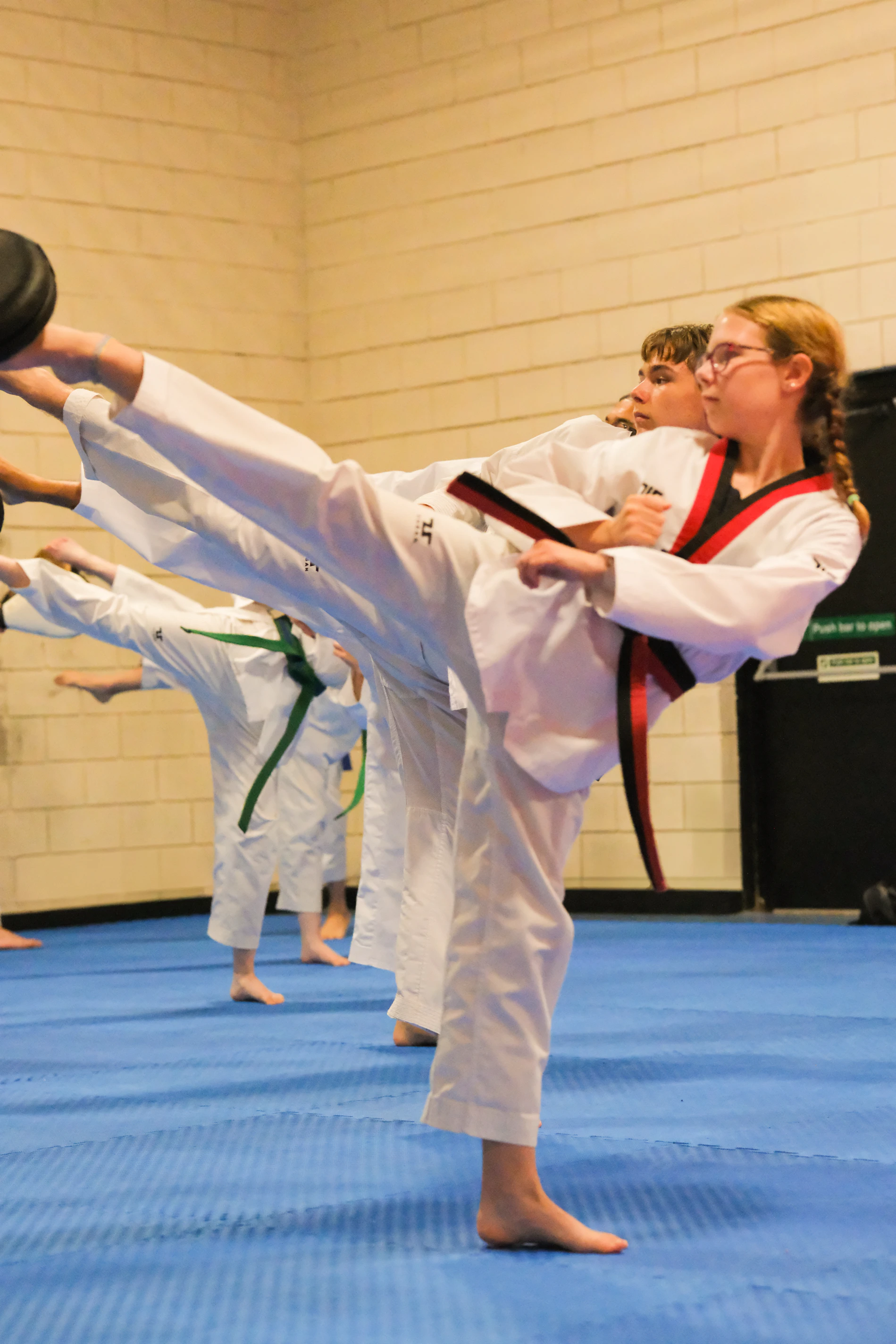 Red belt students practising high kicks during advanced training